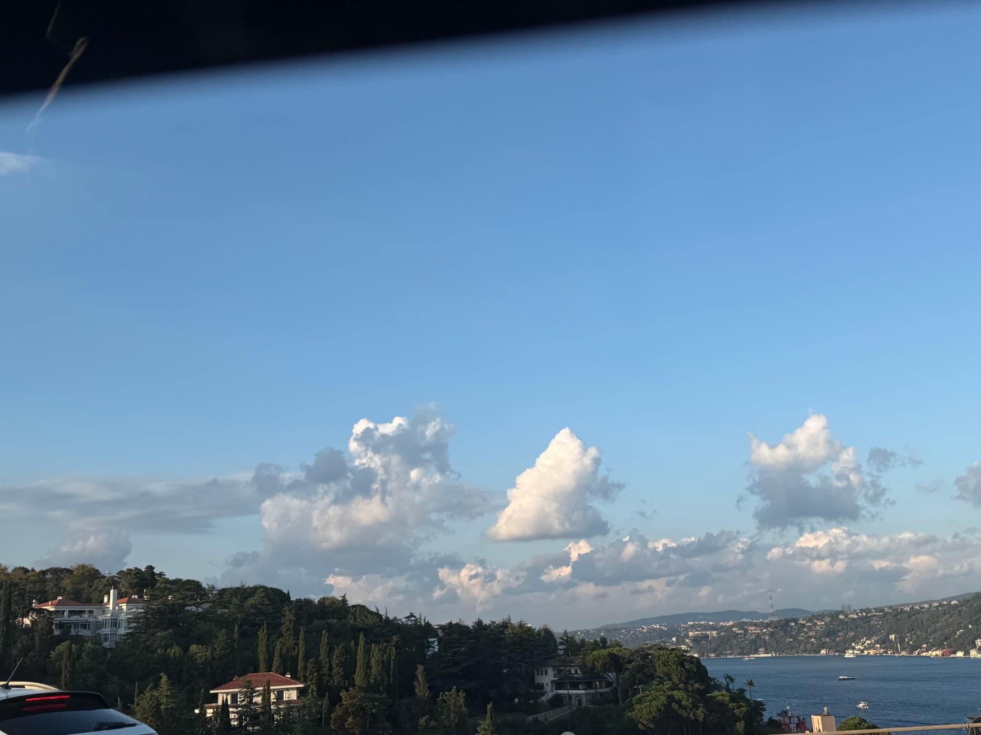 View from a car window of tall clouds over wooded hills and the Bosphorus.