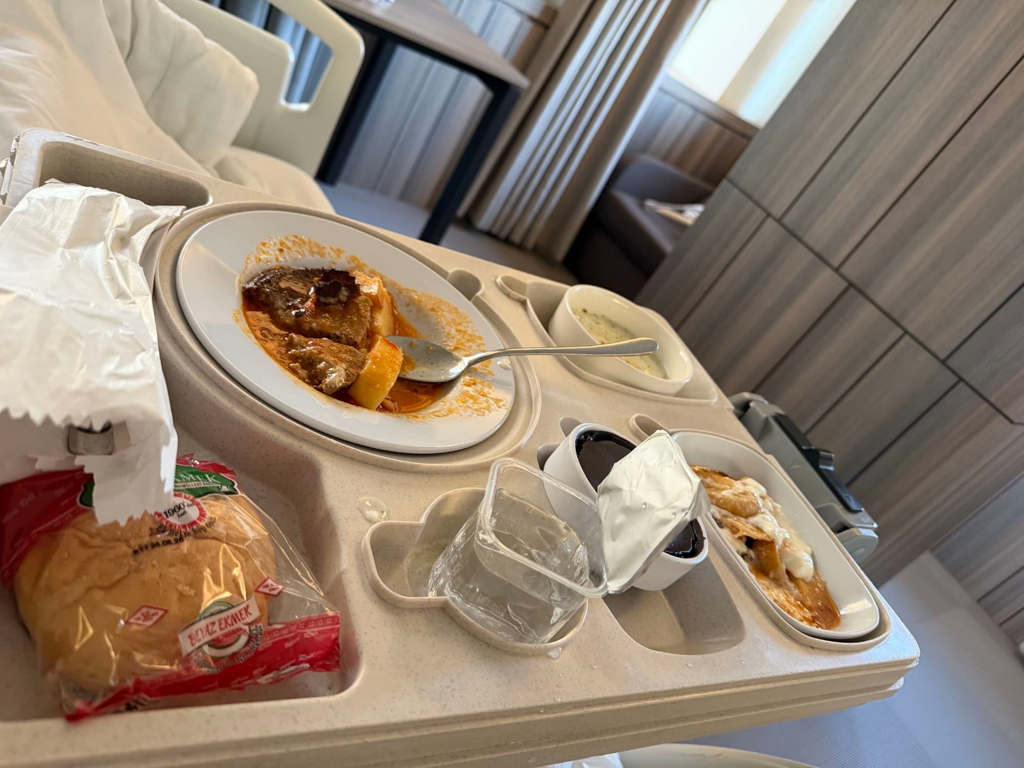 A meal tray with stewed meat and potatoes, soup, bread, and dessert.