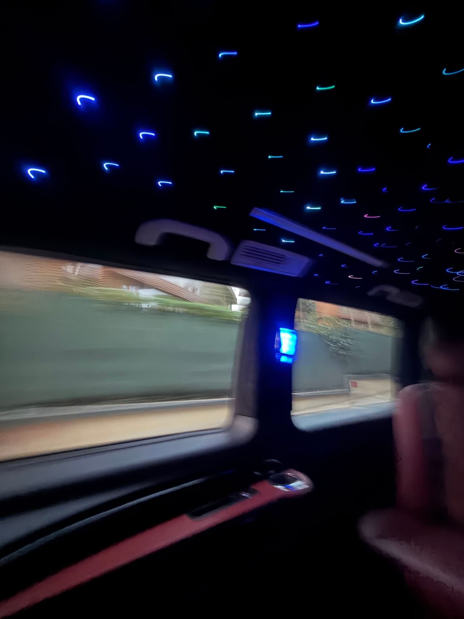Blurred view of the inside of a car with a starlight ceiling, city passing outside the windows.